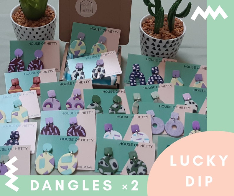 May include: A collection of colorful, geometric patterned polymer clay earrings on display cards. The cards are labeled "House of Hetty" and the earrings are arranged in a random assortment. The text "Lucky Dip" and "Dangles x 2" are visible in the image.