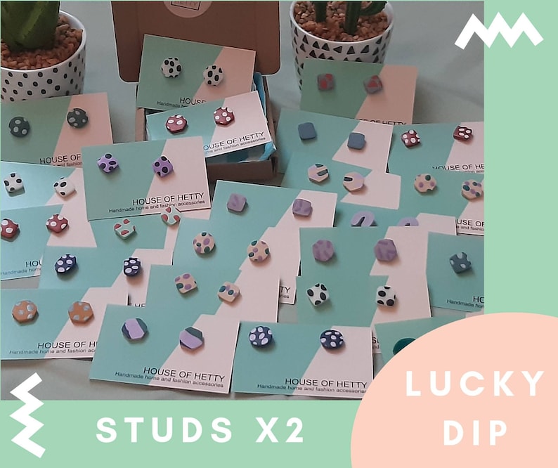May include: A collection of colorful, patterned polymer clay earrings on display. The earrings are arranged on cards with the text "House of Hetty" and "Lucky Dip" on them. The earrings are available in a variety of colors and patterns, including polka dots, stripes, and geometric shapes.