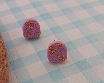 May include: A pair of pink stud earrings with gold flecks. The earrings are small and round, and they have a textured surface.