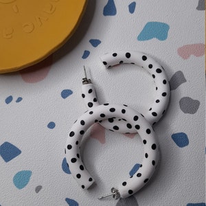 May include: A pair of white hoop earrings with black polka dots. The earrings are made of a thick, rounded material.
