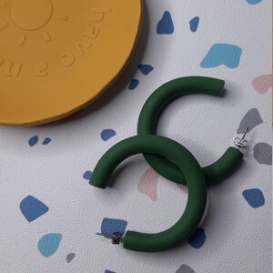 May include: A pair of large, green hoop earrings. The earrings are made of a thick, round material and have a simple, modern design.