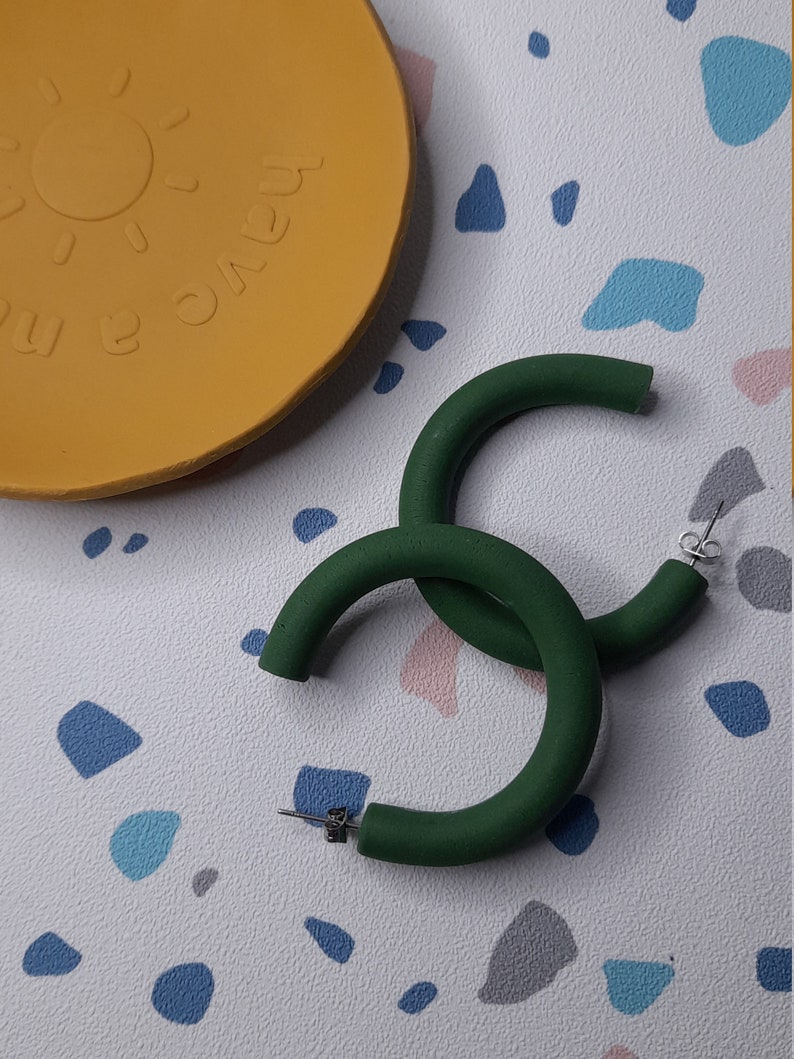 May include: A pair of large, green hoop earrings. The earrings are made of a thick, round material and have a simple, modern design.