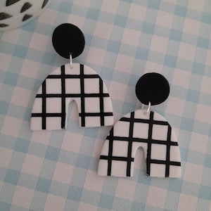 May include: A pair of white and black checkered arch-shaped earrings with black circle accents.