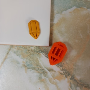 May include: Two geometrically shaped, 3D printed objects. One is orange and the other is yellow. Both are shaped like a pointed crystal.