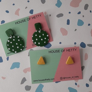 May include: Two sets of earrings on cards with the text "HOUSE OF HETTY" and website information. The first set is green with white polka dots and a small green square. The second set is yellow triangles.