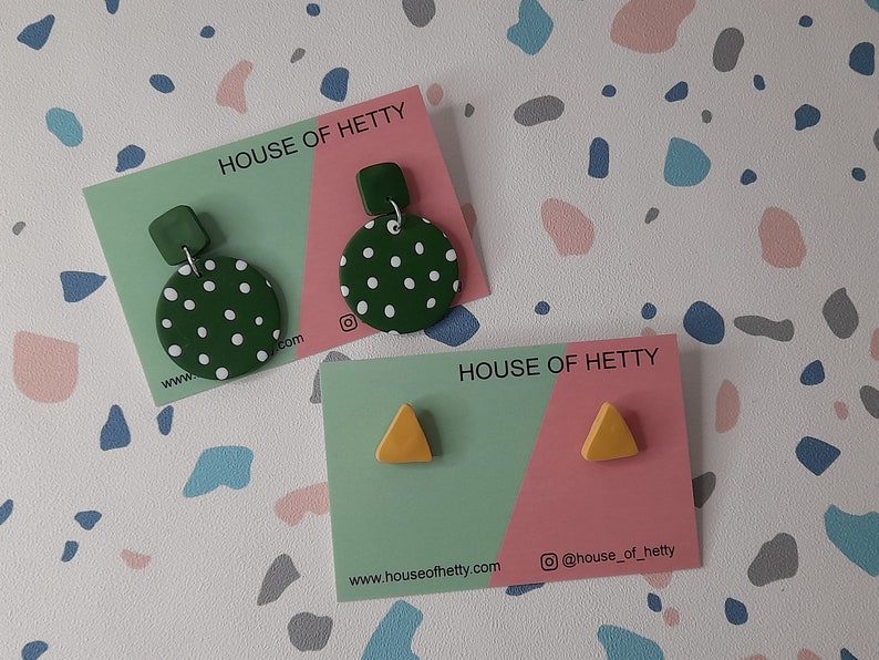May include: Two sets of earrings on cards with the text "HOUSE OF HETTY" and website information. The first set is green with white polka dots and a small green square. The second set is yellow triangles.