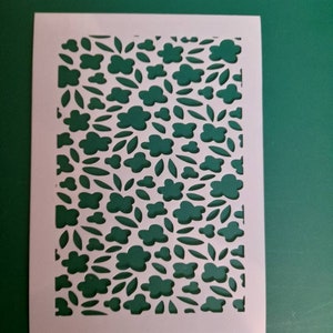 May include: White stencil featuring a repeating pattern of small flowers and leaves. The stencil is cut out to allow for painting or other decorative techniques.