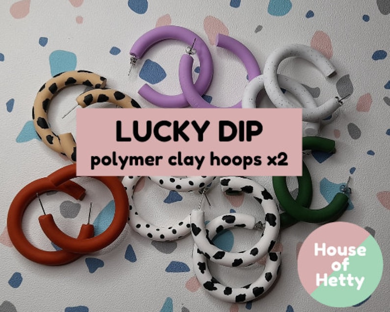 May include: A set of eight colorful polymer clay hoop earrings in various patterns, including leopard print, polka dots, and cow print. The earrings are arranged on a white and gray tiled surface. The text "LUCKY DIP polymer clay hoops x2" is displayed on a pink banner. The text "House of Hetty" is displayed on a pink and green circle.