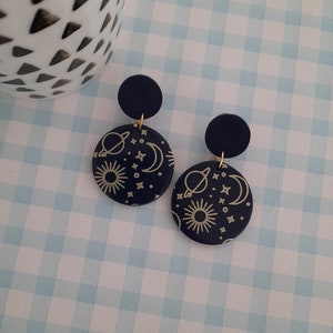 May include: A pair of navy blue earrings with gold celestial designs, including planets, stars, and a crescent moon.