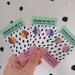 May include: Three cards with a black and white polka dot pattern. Each card features a pair of handmade polymer clay earrings. The earrings are in various colors, including pink, blue, yellow, and green. The cards also include the text "HOUSE OF HETTY" and social media information.