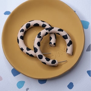 May include: A pair of hoop earrings with a black and white animal print design. The earrings are on a yellow plate.