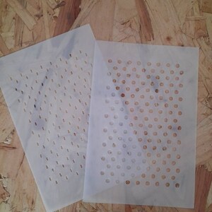 May include: Two white plastic stencils with different patterns of small circles. The stencil on the left has a grid pattern of circles, while the stencil on the right has a diagonal pattern of circles.