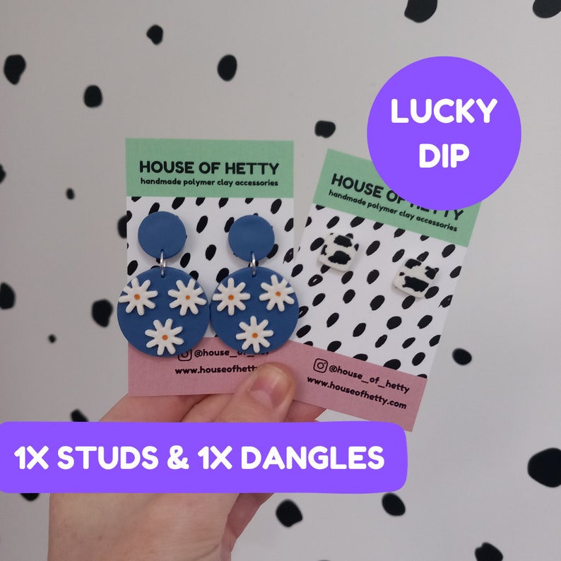 May include: Two pairs of handmade polymer clay earrings. One pair features blue and white daisy flower dangles. The other pair features black and white cow print studs. The cards have the text "House of Hetty" and "Lucky Dip".