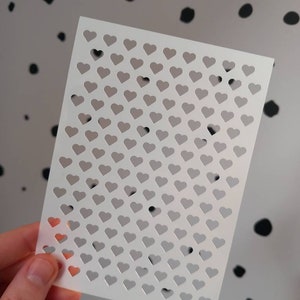 May include: White stencil sheet with a grid of small heart cutouts.