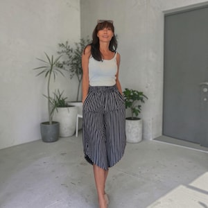 May include: A white sleeveless tank top paired with high-waisted, wide-leg culottes featuring a vertical black and white pinstripe pattern. The trousers have an elasticated waistband and a loose, flowing silhouette that falls below the knees.