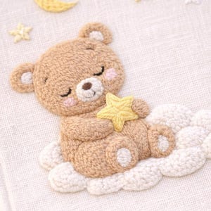 May include: Embroidered artwork featuring a sleeping teddy bear holding a yellow star, resting on a white cloud. A yellow crescent moon and stars are in the background. The bear is light brown with pink cheeks.