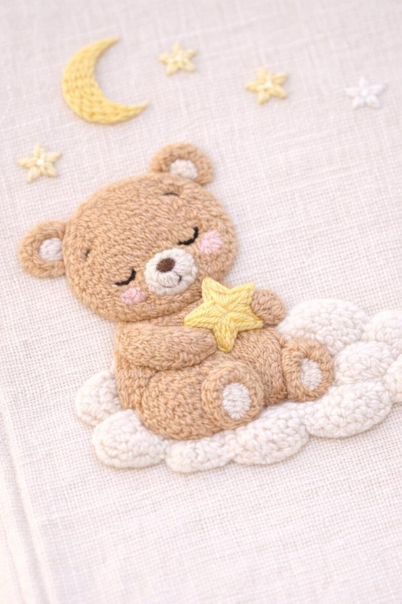 May include: Embroidered artwork featuring a sleeping teddy bear holding a yellow star, resting on a white cloud. A yellow crescent moon and stars are in the background. The bear is light brown with pink cheeks.