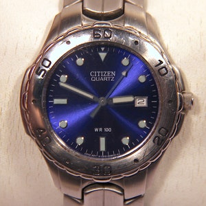 May include: A silver Citizen Quartz wristwatch with a blue face and silver hands. The watch has a silver band and a black bezel with white numbers. The watch is water resistant to 100 meters.