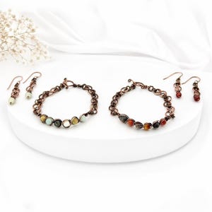 Può includere: Due set di gioielli abbinati, ciascuno con un braccialetto a catena color rame e un paio di orecchini. I braccialetti sono adornati con pietre preziose colorate e lucide. Gli orecchini hanno un design simile, con piccole perle di pietre preziose.