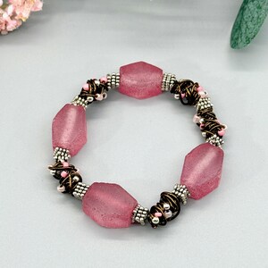 Peut inclure: Un bracelet composé de quatre grosses perles hexagonales rose translucide alternant avec des sections de fil de bronze foncé enroulées autour de petites perles de rocaille argentées et rose clair, avec des intercalaires argentés.