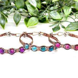May include: Three copper wire bracelets with colorful gemstone beads. The bracelets feature purple, teal, and pink beads. The jewelry is displayed against a white background with green foliage.