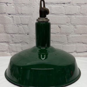 May include: A vintage green pendant light fixture with a rounded shade and a dark metal hanging loop. The shade has a glossy finish and a cylindrical top section. The fixture is against a white brick wall.
