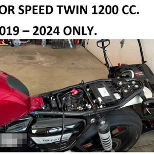 Puede incluir: Primer plano de una motocicleta negra con un tanque de gasolina rojo y un asiento negro. La motocicleta tiene un tubo de escape cromado y un guardabarros trasero negro. La motocicleta est&aacute; en un garaje y el texto "SPEED TWIN" es visible en el lateral de la motocicleta.