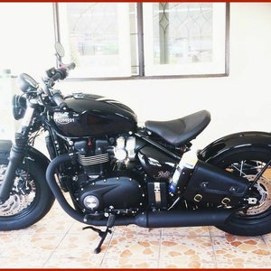 May include: A black Triumph motorcycle with a black leather saddlebag. The motorcycle has a chrome exhaust pipe and a black seat.