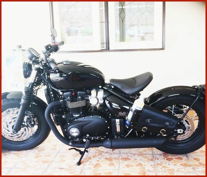 May include: A black Triumph motorcycle with a black leather saddlebag. The motorcycle has a chrome exhaust pipe and a black seat.