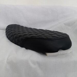 May include: Black quilted motorcycle seat with a diamond pattern. The seat is made of leather and has a smooth, rounded edge.