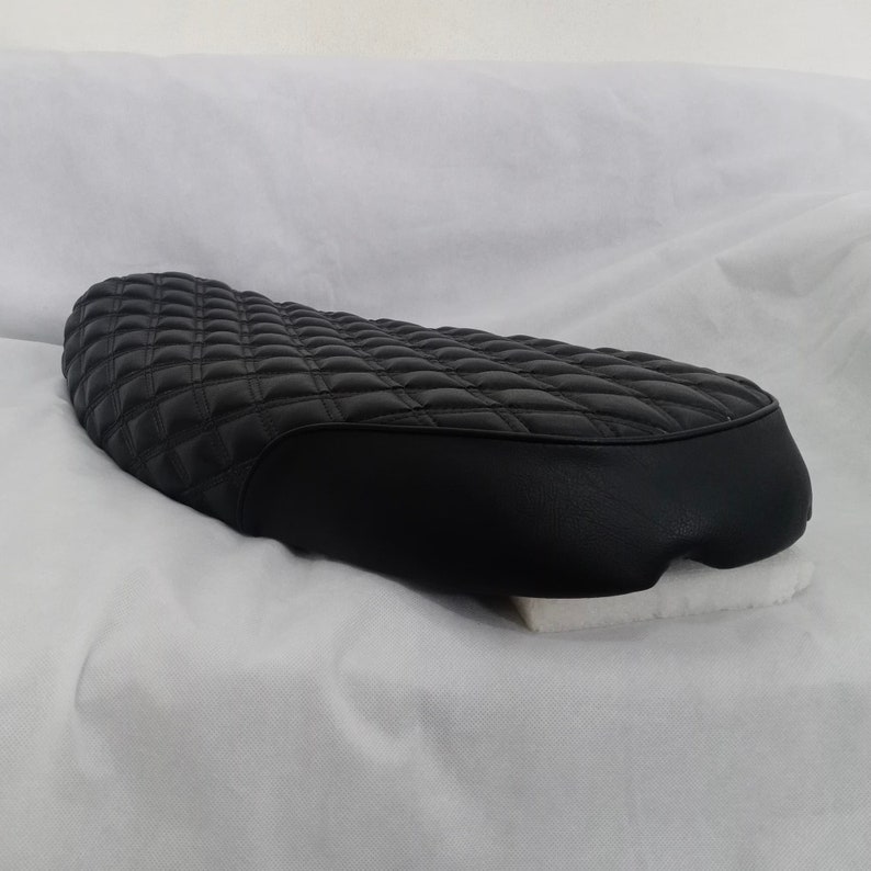 May include: Black quilted motorcycle seat with a diamond pattern. The seat is made of leather and has a smooth, rounded edge.