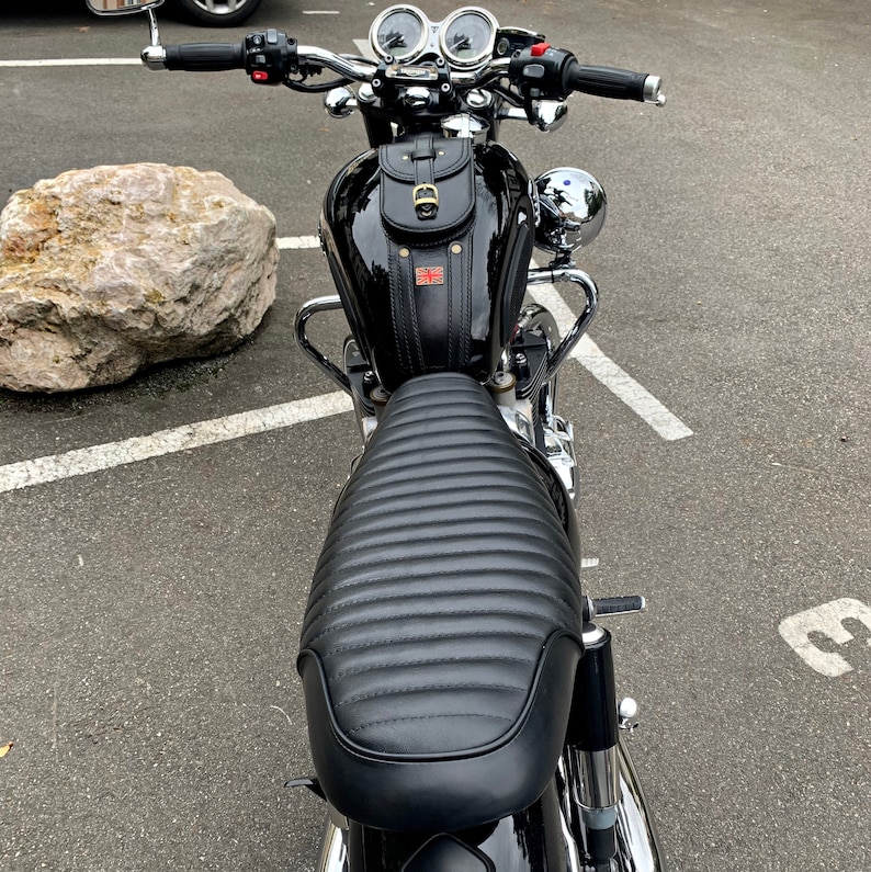 K&ouml;nnte beinhalten: Schwarzes Motorrad mit einem schwarzen Ledersitz und einer schwarzen Ledertasche. Das Motorrad hat verchromte Lenker, Spiegel und Auspuffrohre.