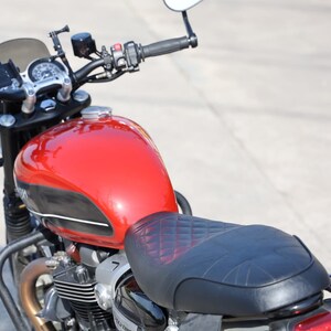 Puede incluir: Una motocicleta roja con un asiento negro y una franja negra y blanca en el tanque de gasolina. La motocicleta tiene un parabrisas negro y un guardabarros trasero cromado.