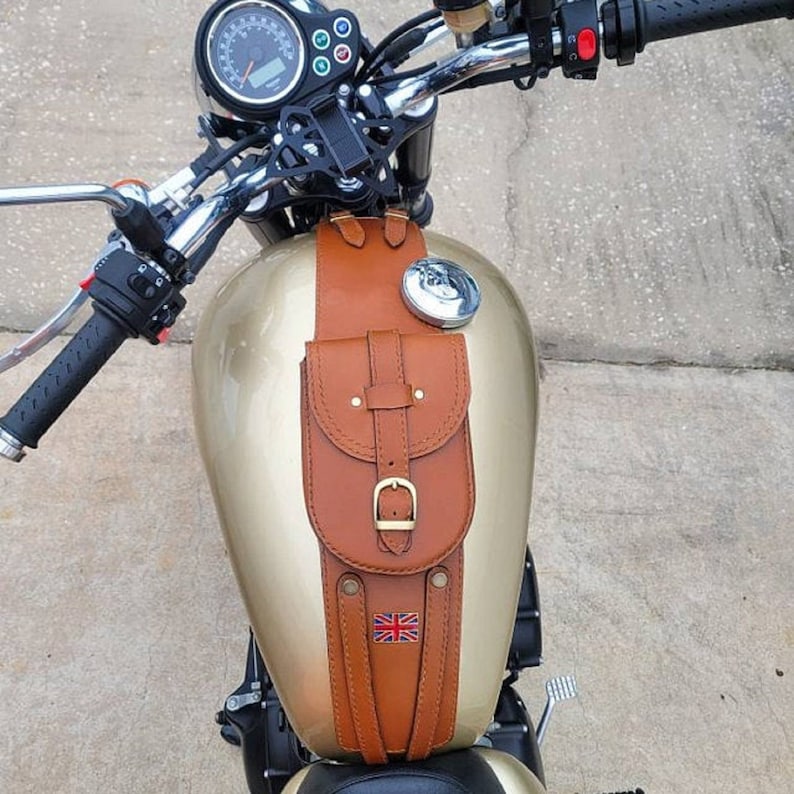 K&ouml;nnte beinhalten: Eine braune Leder-Motorrad-Tanktasche mit einer Schnallenverschluss und einem Union-Jack-Design. Die Tasche ist an einem Motorrad-Benzintank befestigt.