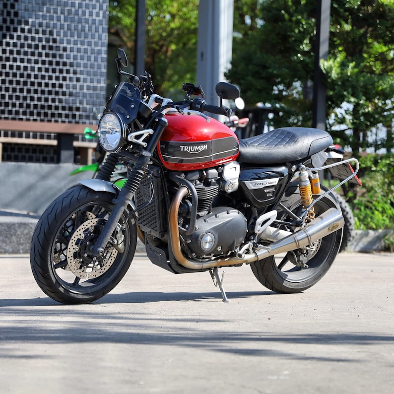 Puede incluir: Una motocicleta Triumph roja con detalles negros y un asiento de cuero negro. La motocicleta tiene un parabrisas negro y un tubo de escape cromado.