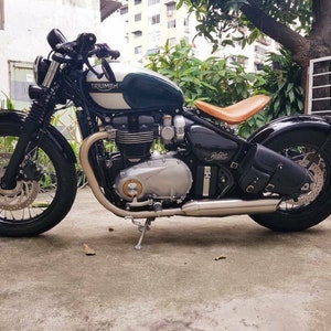 May include: A green and black Triumph motorcycle with a brown leather seat. The motorcycle has a chrome exhaust pipe and a black leather saddlebag.