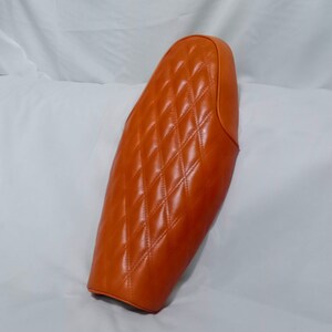 May include: Orange quilted motorcycle seat with a diamond pattern.