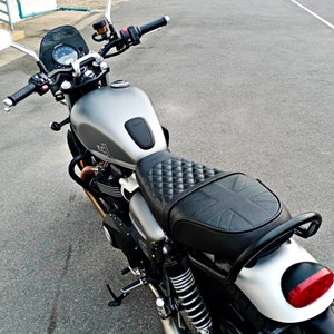 Puede incluir: Una motocicleta plateada con un asiento de cuero negro y un patr&oacute;n de Union Jack. La motocicleta tiene un manillar negro y un faro negro.