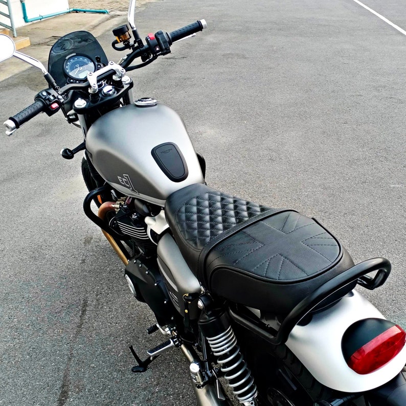 Puede incluir: Una motocicleta plateada con un asiento de cuero negro y un patr&oacute;n de Union Jack. La motocicleta tiene un manillar negro y un faro negro.