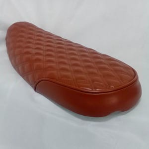 May include: A brown quilted motorcycle seat with a rounded edge.