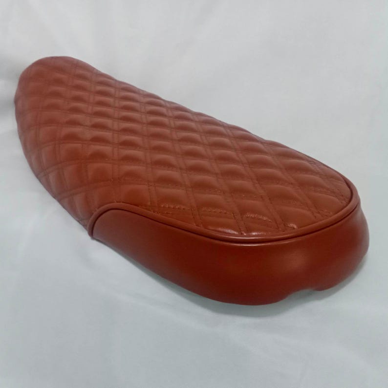May include: A brown quilted motorcycle seat with a rounded edge.