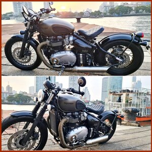 May include: A black Triumph motorcycle with a brown leather seat and chrome accents. The motorcycle is parked on a concrete surface with a city skyline in the background.