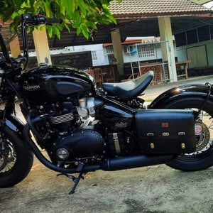 May include: A black Triumph motorcycle with a black leather saddlebag. The motorcycle has a chrome exhaust and a black seat.