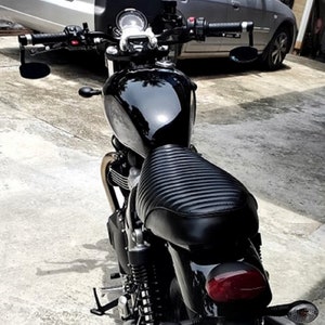 Puede incluir: Una motocicleta negra con un asiento de cuero negro y detalles cromados. La motocicleta tiene un faro redondo y un manillar negro con espejos.