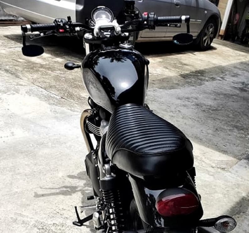 Puede incluir: Una motocicleta negra con un asiento de cuero negro y detalles cromados. La motocicleta tiene un faro redondo y un manillar negro con espejos.