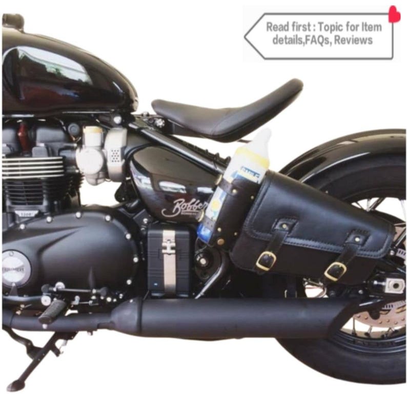 May include: Black motorcycle with a brown leather saddlebag attached to the rear fender. The saddlebag has two buckles and a strap. A clear plastic bottle is secured to the saddlebag with a strap.