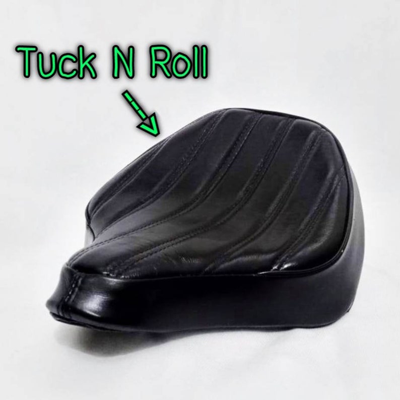 May include: Black leather motorcycle seat with a tuck and roll design. The seat has a stitched pattern and is designed for a solo rider.