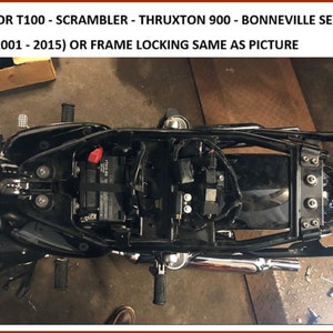 May include: A black motorcycle frame with a battery, wiring, and exhaust system. The text "FOR T100 - SCRAMBLER - THRUXTON 900 - BONNEVILLE SE (2001 - 2015) OR FRAME LOCKING SAME AS PICTURE" is visible in the image.
