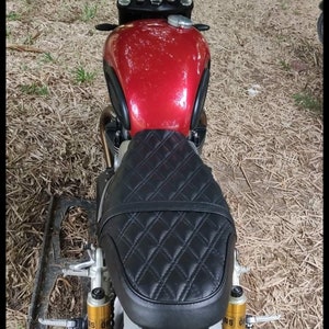 May include: A red motorcycle with a black quilted seat and gold shocks. The motorcycle has a black handlebar and mirrors.