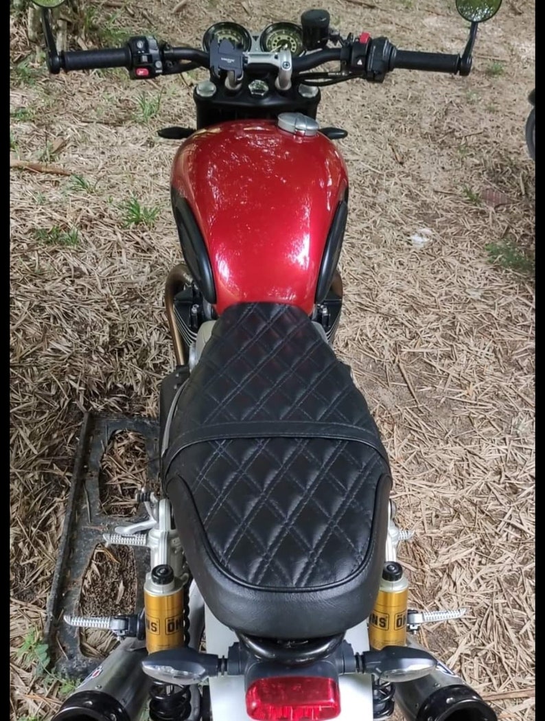 May include: A red motorcycle with a black quilted seat and gold shocks. The motorcycle has a black handlebar and mirrors.